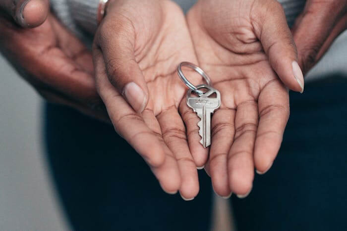 Deux mains se tenant avec précaution, l'une tenant une clé de maison. La clé symbolise la propriété et l'acquisition d'un nouveau logement, illustrant le concept de l'investissement immobilier et de l'accès à la propriété.