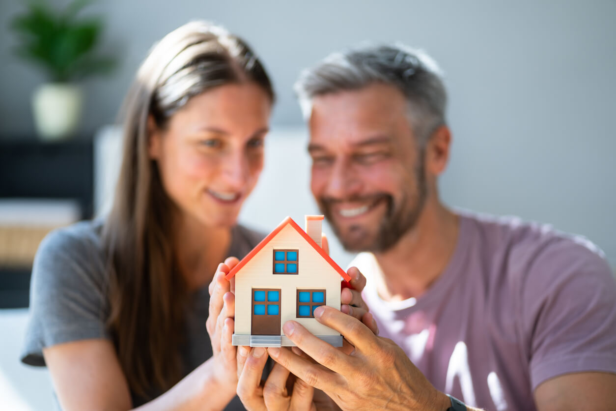 Couple tenant une illustration de maison, symbolisant la création d'une SCI en couple. Découvrez les 4 étapes clés pour réussir votre projet immobilier en SCI, de la définition du projet à l'achat du bien.