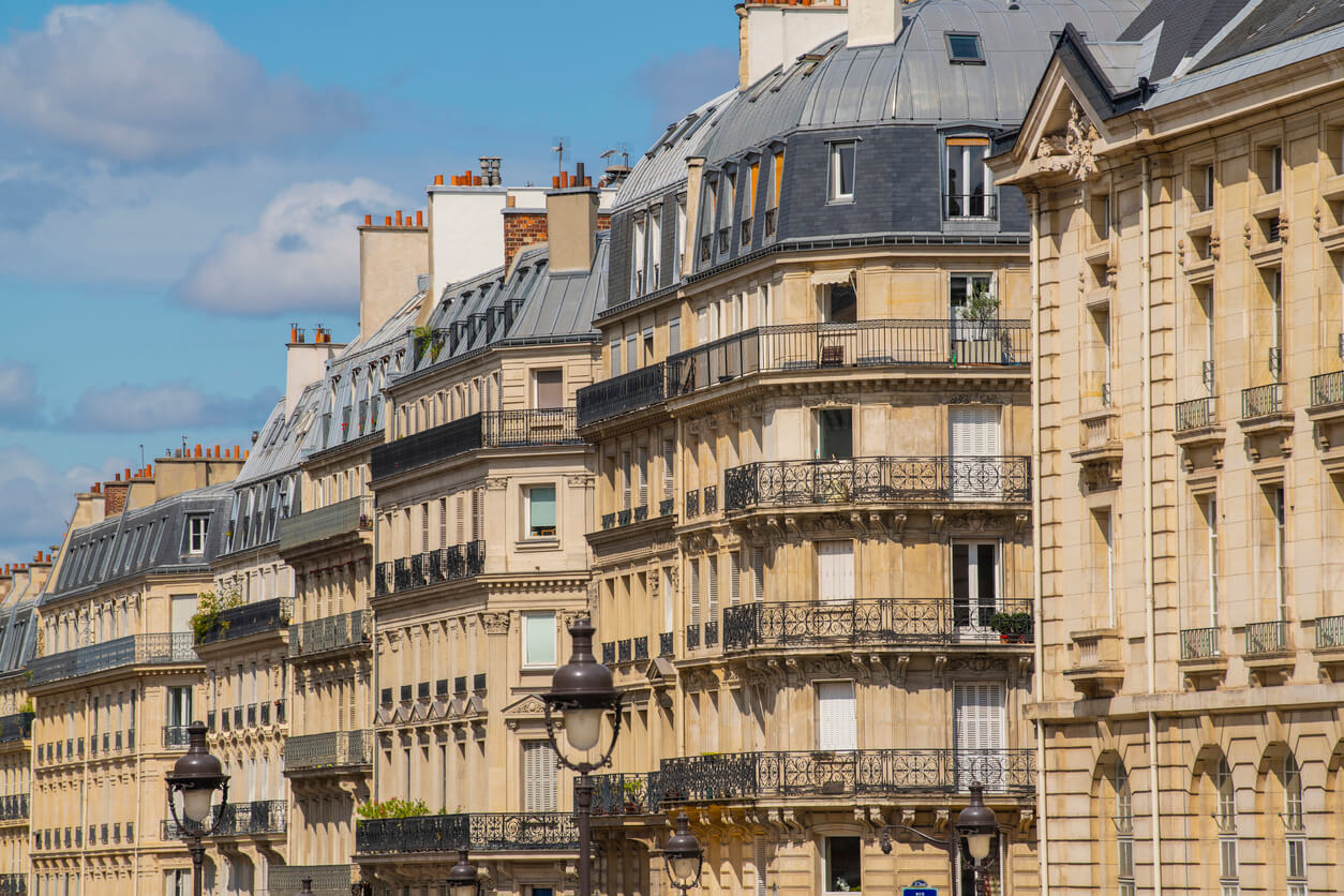 Vue d’immeubles parisiens sous un ciel clair, illustrant l’application de la taxe d'habitation pour les biens détenus par une SCI en zone urbaine, avec des conditions spécifiques d’exonération et de majoration selon l’usage et la localisation des biens.