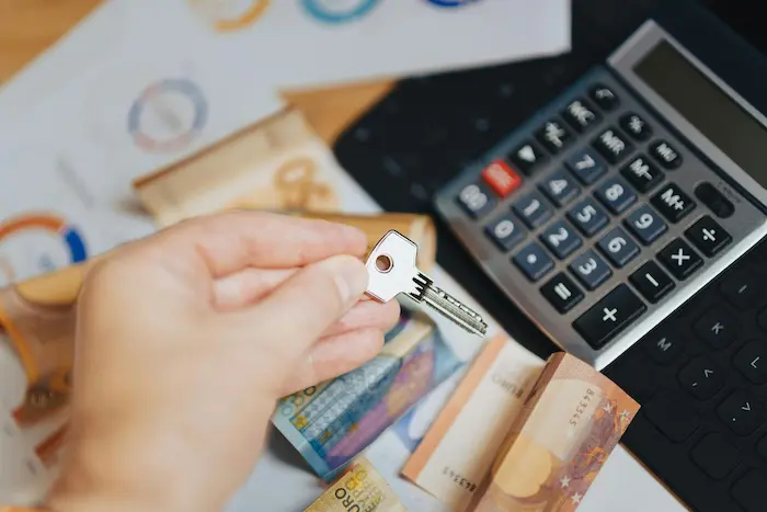 Main tenant une clé au-dessus de billets d’euros, illustrant l’importance de l’apport personnel pour sécuriser un achat immobilier.