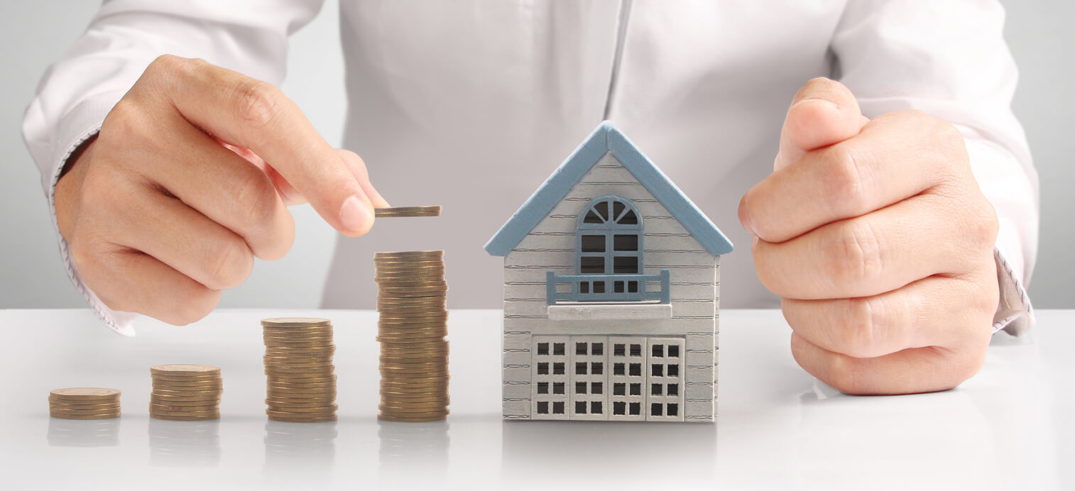 Une main empile des pièces près d'une maquette de maison. La photo symbolise l'investissement immobilier et la gestion financière en Société Civile Immobilière