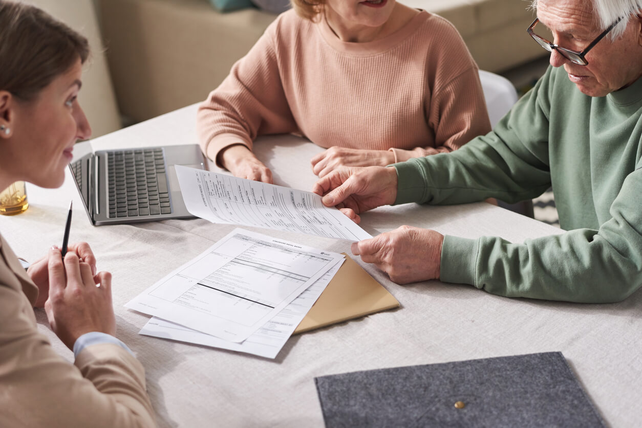 Trois personnes échangent autour d'une table, analysant des documents fiscaux relatifs à l'assurance-vie en cas de décès.