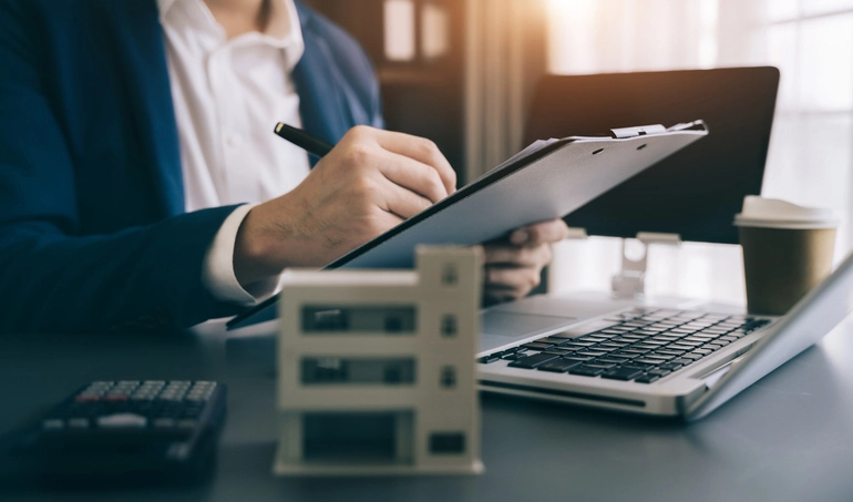 Une personne travaillant à son bureau, avec une maquette de bien immobilier, qui montre un chargé de gestion locative auquel est confié de nombreuses tâches.