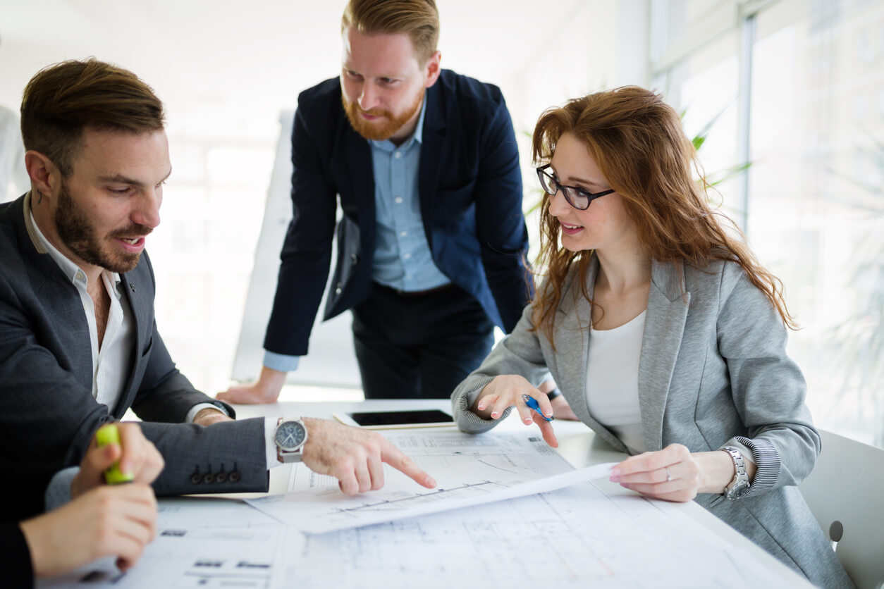 Image de trois personnes dans un bureau, travaillant sur des dossiers et un ordinateur, symbolisant des conseils et stratégies pour réussir son investissement en SCPI