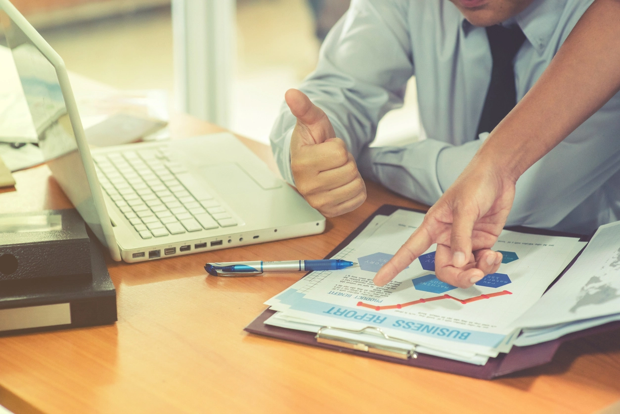 Deux personnes en tenue professionnelle discutent autour d'un bureau, analysant un rapport des frais d'agence gestion locative avec des graphiques