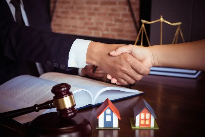 Deux personnes se serrent la main devant gavel, balance et maisons miniatures, symbolisant calcul des frais de notaire dans le neuf via simulateur.