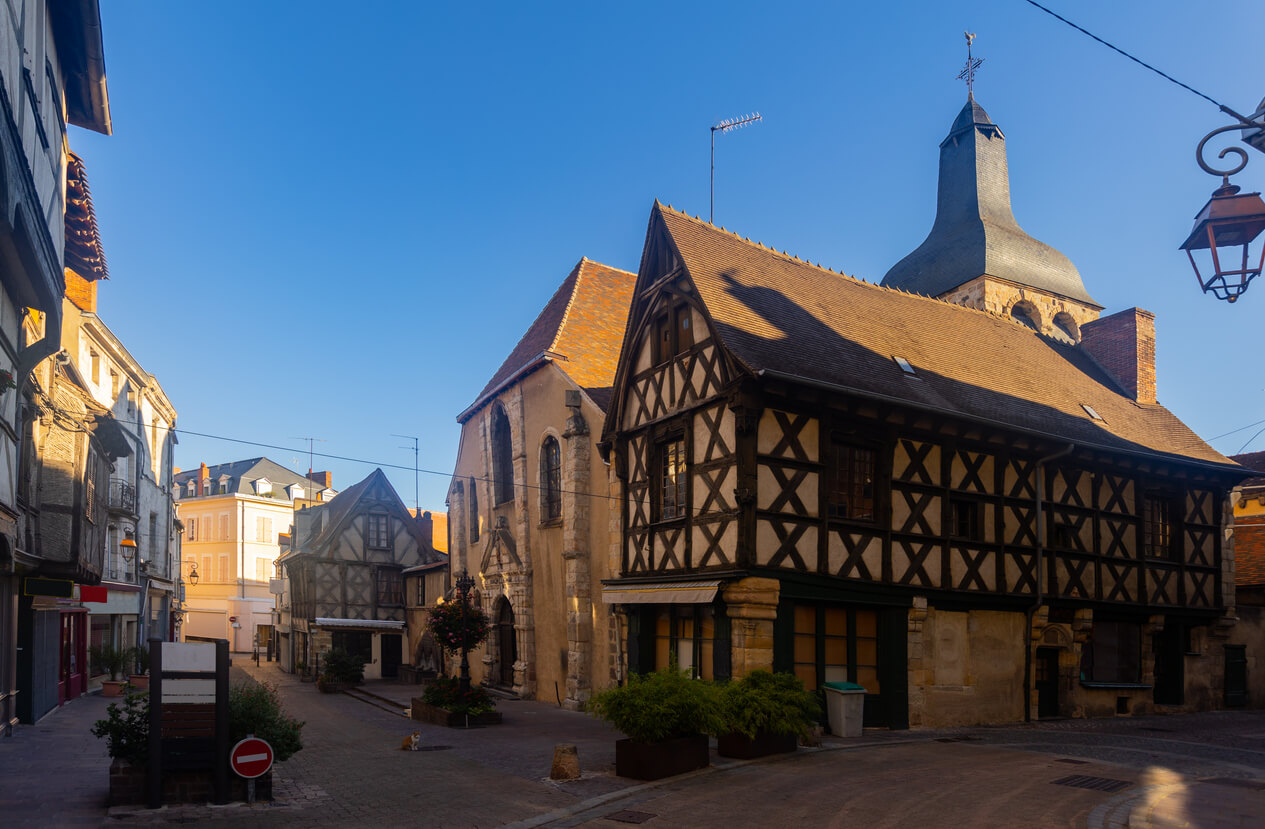 Vue pittoresque du centre historique avec maisons à colombages et une église, illustrant l'attrait de l'investissement locatif Montluçon