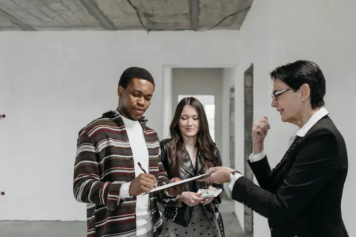 Trois personnes réunies dans pièce claire, l’une signe un document sur clipboard, illustrant la signature d’un contrat de location vide.