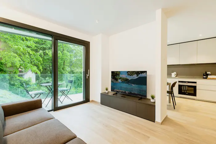 Salon moderne avec cuisine ouverte et balcon verdoyant, image représentant l’achat d’un appartement T3 neuf lumineux et fonctionnel.