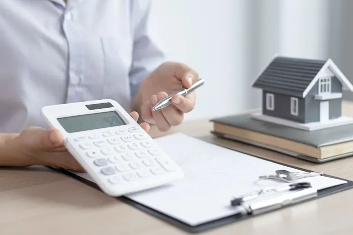 Personne tenant une calculatrice et un stylo, illustrant la simulation de financement immobilier pour évaluer la faisabilité d’un projet d’achat.