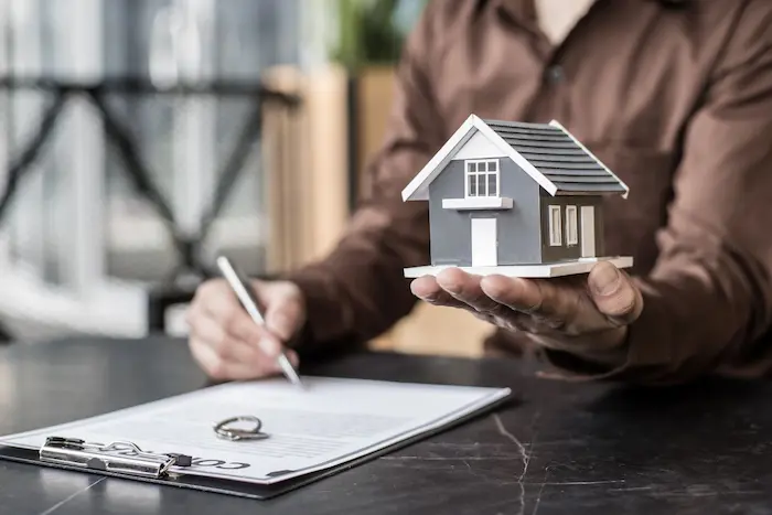 Personne tenant une maquette de maison et signant un contrat, image qui illustre le calcul et l’importance du rendement locatif.