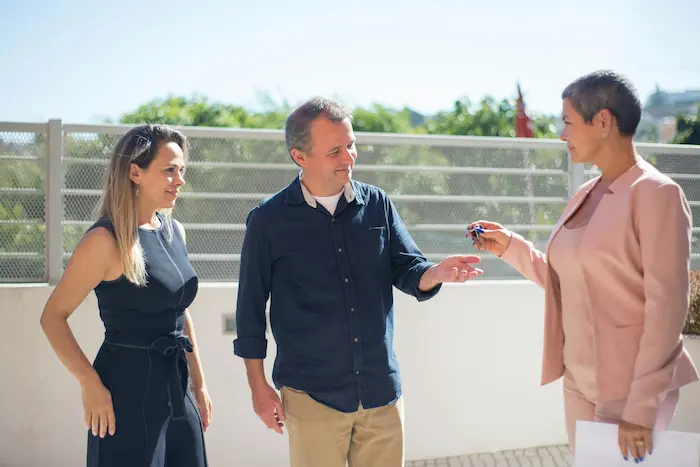 Courtier en costume rose remettant clés à clients, image illustrant le rôle du courtier prêt immobilier 