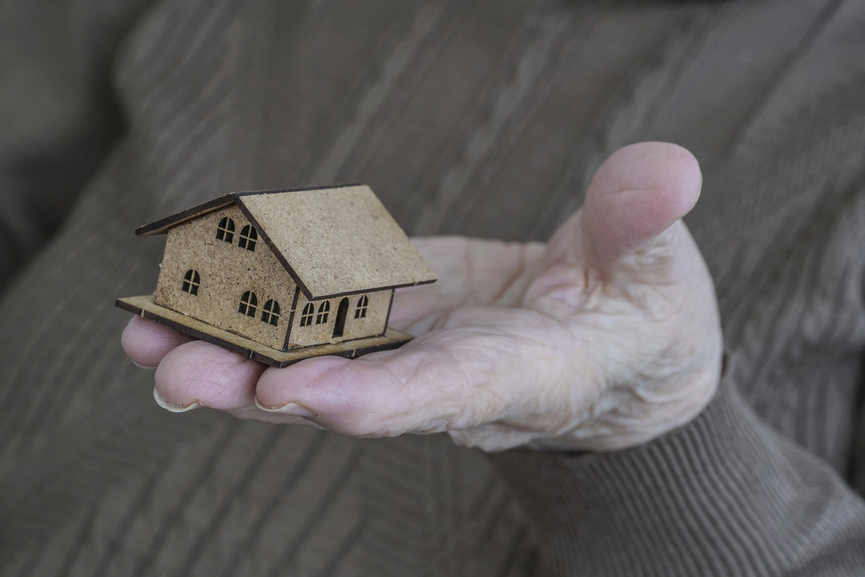 Une main tient une maison miniature, symbolisant le transfert de biens