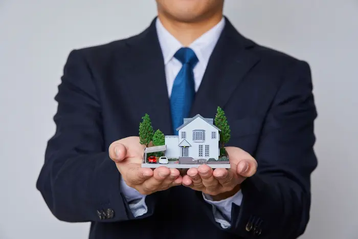Personne en costume tenant une maquette de maison, image illustrant l’accompagnement d’un courtier pour obtenir un prêt immobilier sans apport.