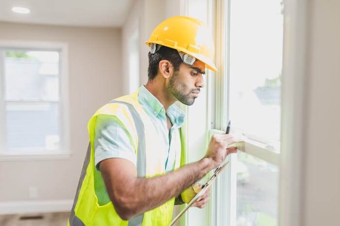 Un homme en tenue de travail, portant un casque de sécurité entrain d'améliorer l'isolation d'une maison. 