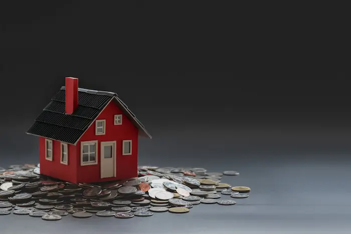 Petite maison rouge posée sur des pièces, image illustrant les conditions du prêt à taux zéro et l’importance de financer un projet immobilier.