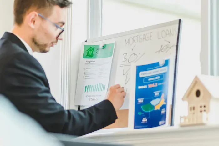 Conseiller en costume devant tableau de prêts, image illustrant le rôle du courtier en assurance prêt immobilier.