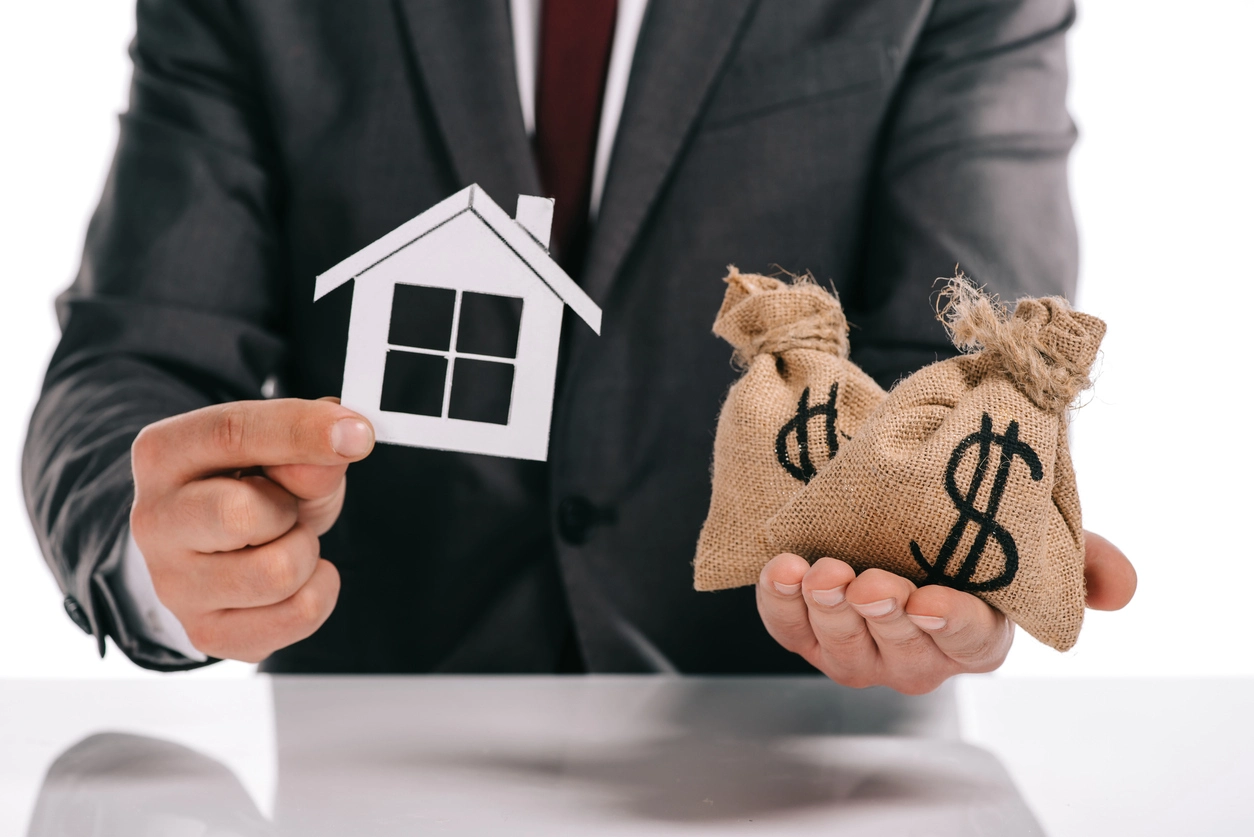 Un homme en costume tient une maison en papier et des sacs d'argent, illustrant le coût et les avantages fiscaux liés à une donation nue propriété