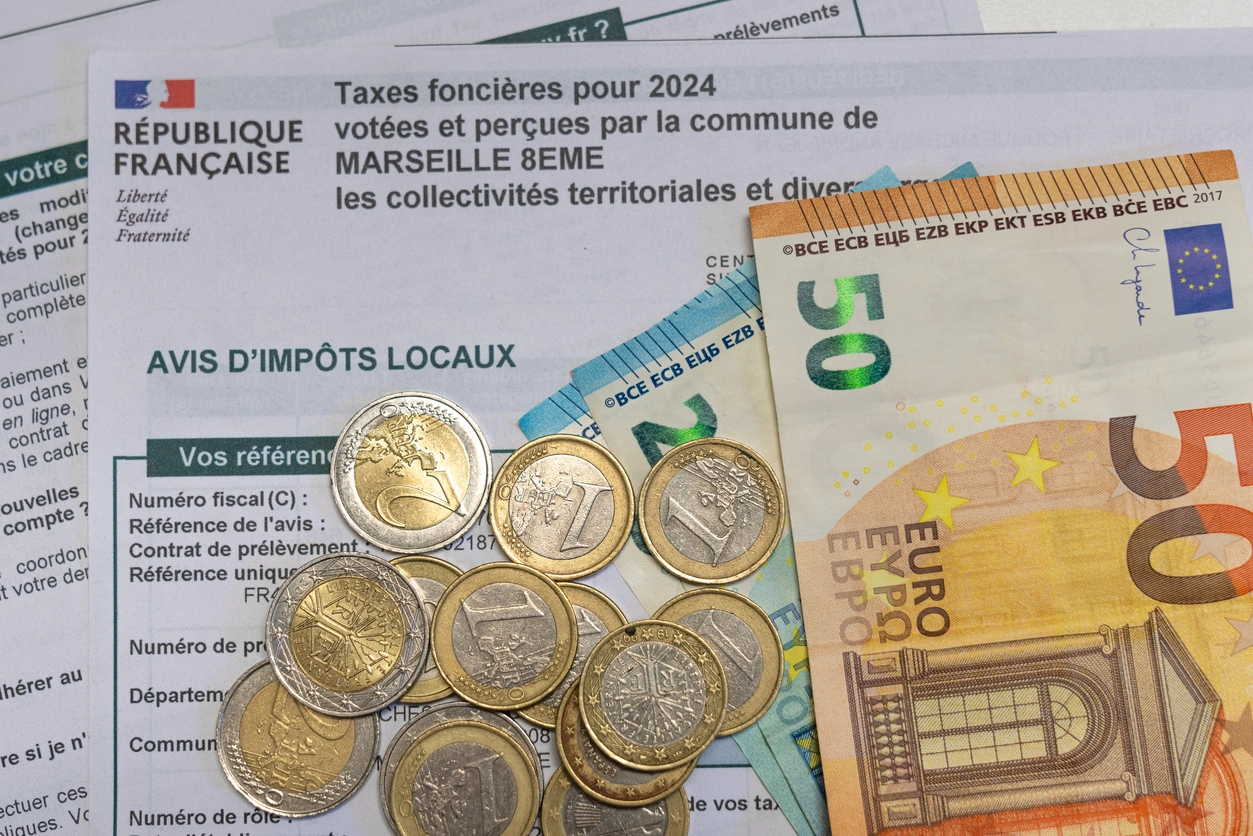 Avis de taxe foncière pour 2024 avec des pièces et billets en euros, symbolisant le paiement des impôts locaux en France.