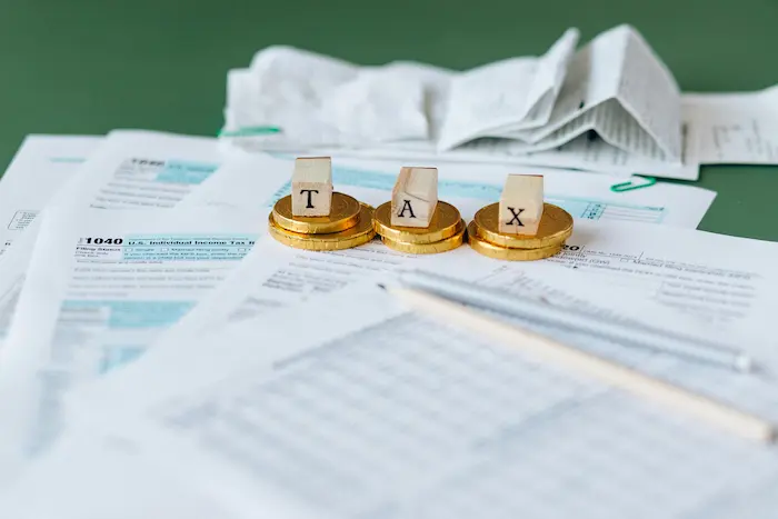 Formulaires fiscaux avec pièces et blocs TAX, image illustrant la taxation de votre plus-value immobilière.