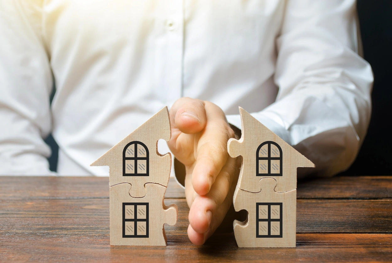 Une main sépare en deux une maison en bois sous forme de puzzle, symbolisant le partage d’un bien immobilier et la succession.