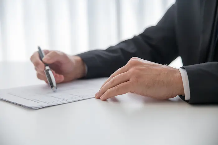 Scène de bureau où un homme en costume remplit sa déclaration LMNP, stylo en main et document imprimé devant lui.