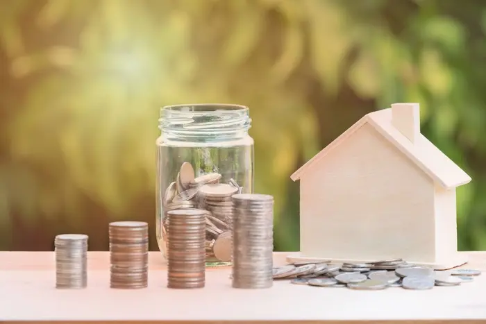 Petite maison en bois posée à côté de piles de pièces de monnaie pour illustrer si l'on peut déduire la taxe foncière des revenus fonciers lors de sa déclaration