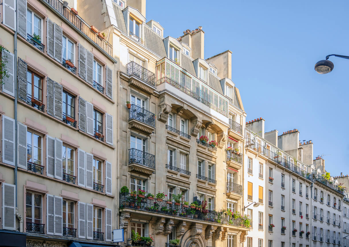 Vue d'un élégant immeuble ancien typiquement français, avec une façade en pierre, des balcons en fer forgé, et des fenêtres à volets. Cet édifice représente le type de bien que l'on pourrait acquérir avec une SCI pour acheter une maison ou un appartement en copropriété. Créer une SCI permettrait ici d’optimiser la gestion et la transmission de ce type de patrimoine immobilier tout en facilitant la répartition des parts entre associés.