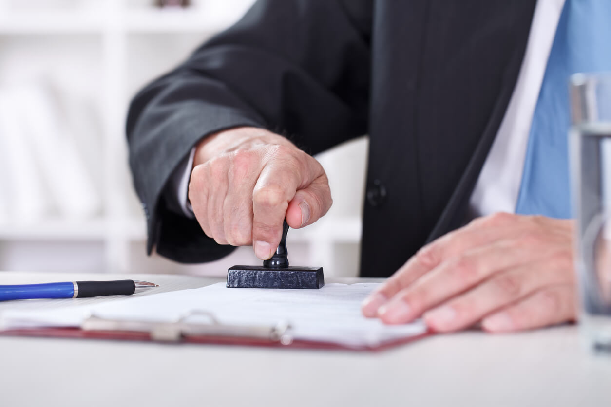 Un homme en costume utilise un tampon pour valider un document officiel. Cette image illustre les démarches administratives et juridiques essentielles, comme celles liées à une SCI familiale succession exemple, pour garantir la conformité et faciliter la gestion du patrimoine