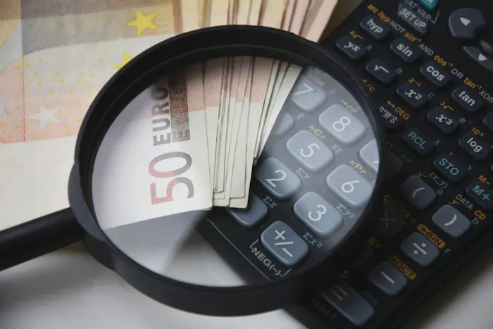 Loupe sur billets et calculatrice scientifique, image illustrant l’analyse des taux de crédit immobilier pour mieux gérer financement.