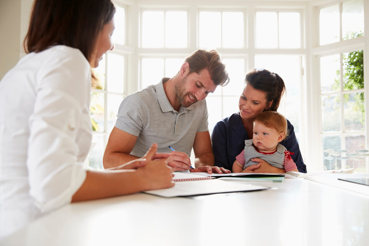 L'image montre une réunion entre un officier public, peut-être un notaire ou un avocat, et une famille (le père, la mère et leur bébé) en train de signer un contrat.