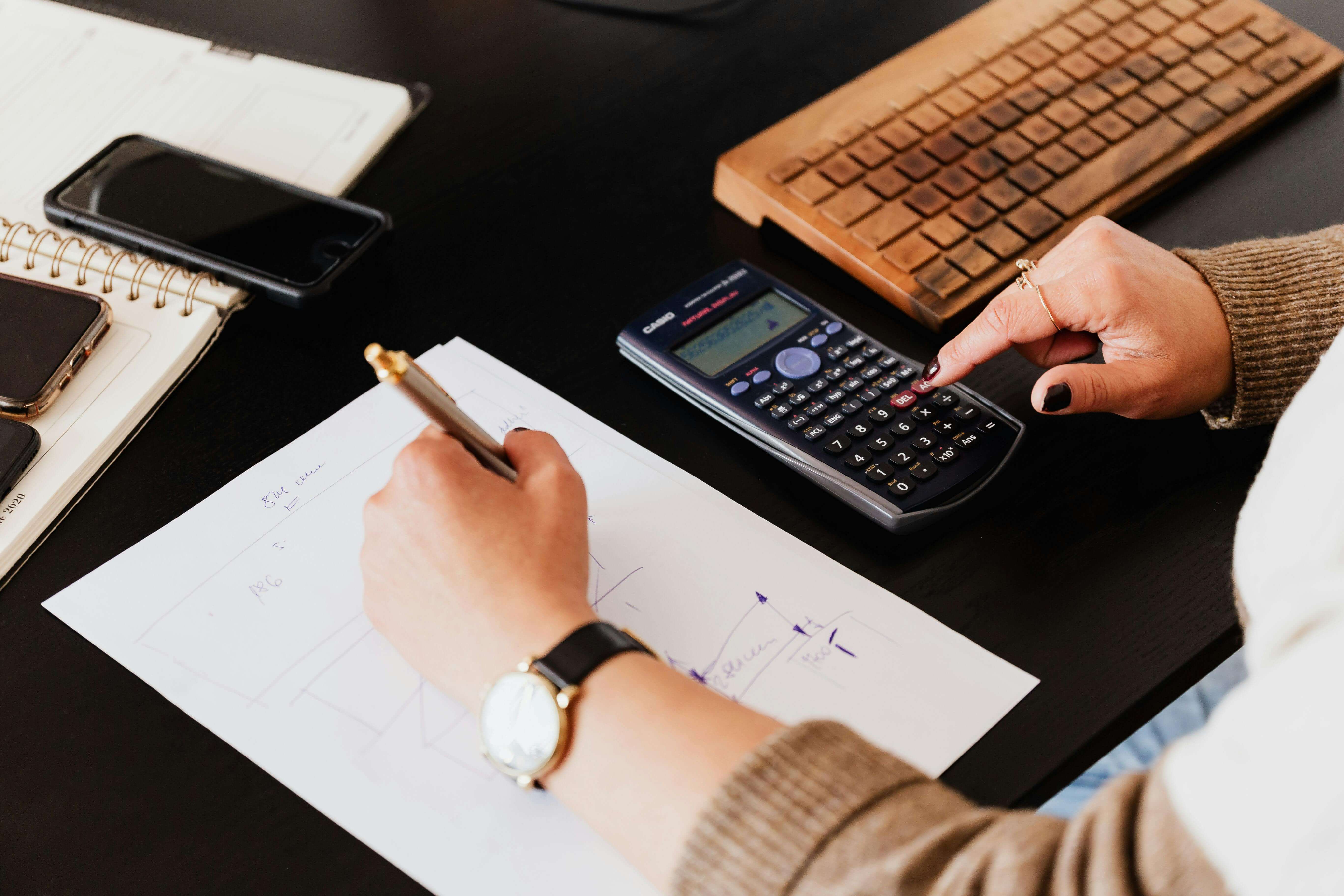 : Personne utilisant une calculatrice avec un cahier et un clavier en arrière-plan pour choisir le régime fiscal SCI