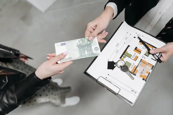 Gros plan sur transaction avec billet de 100 euros remis et plan d’appartement, reflet d’un achat immobilier en cours.