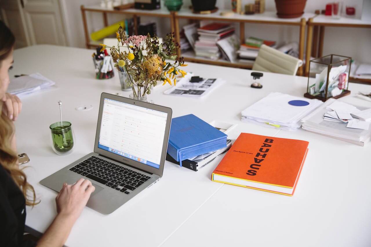 Une femme assise à son bureau, concentrée devant son ordinateur, examinant les détails financiers et administratifs liés au coût de création d'une SCI (Société Civile Immobilière), incluant les frais de notaire, d'expertise et de formalités légales.