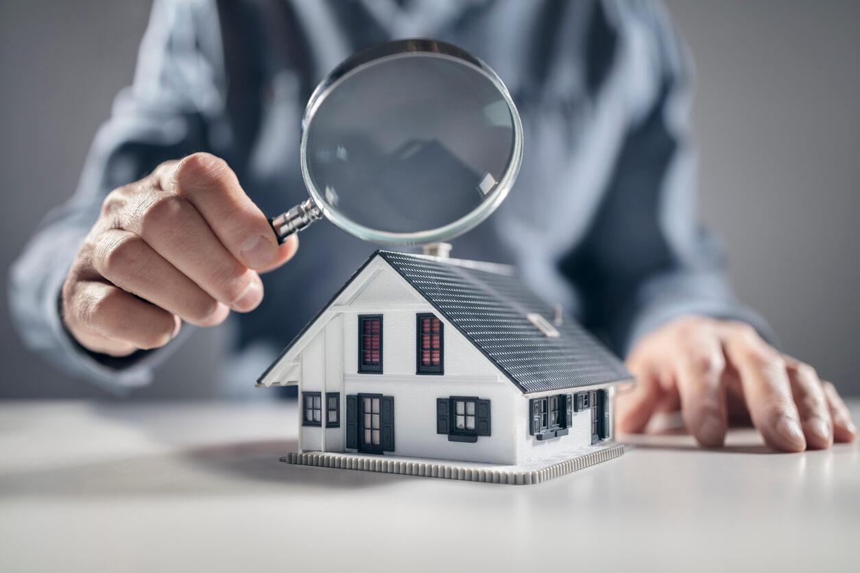 Un homme tient une loupe et inspecte un modèle de maison. L'image reflète l'idée de mettre sa maison en SCI 