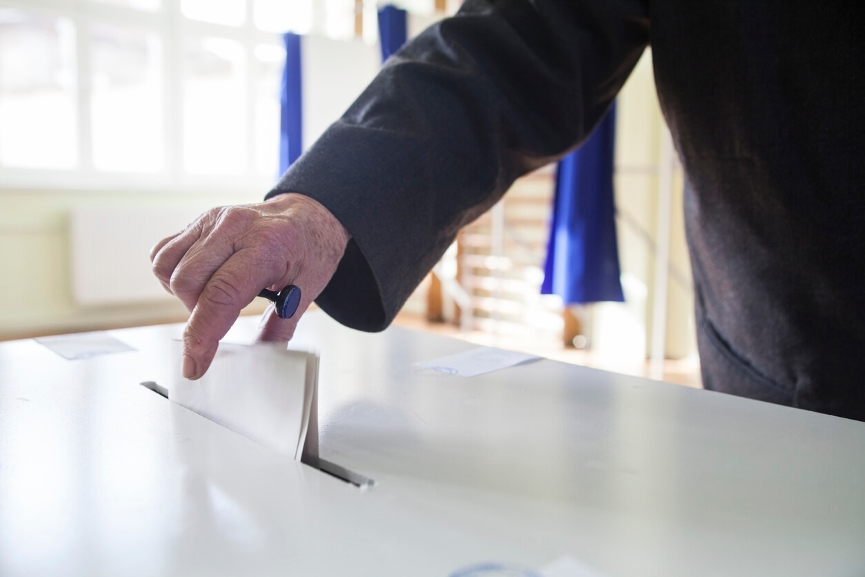 Gros plan sur une main déposant un bulletin de vote plié dans une urne de vote transparente