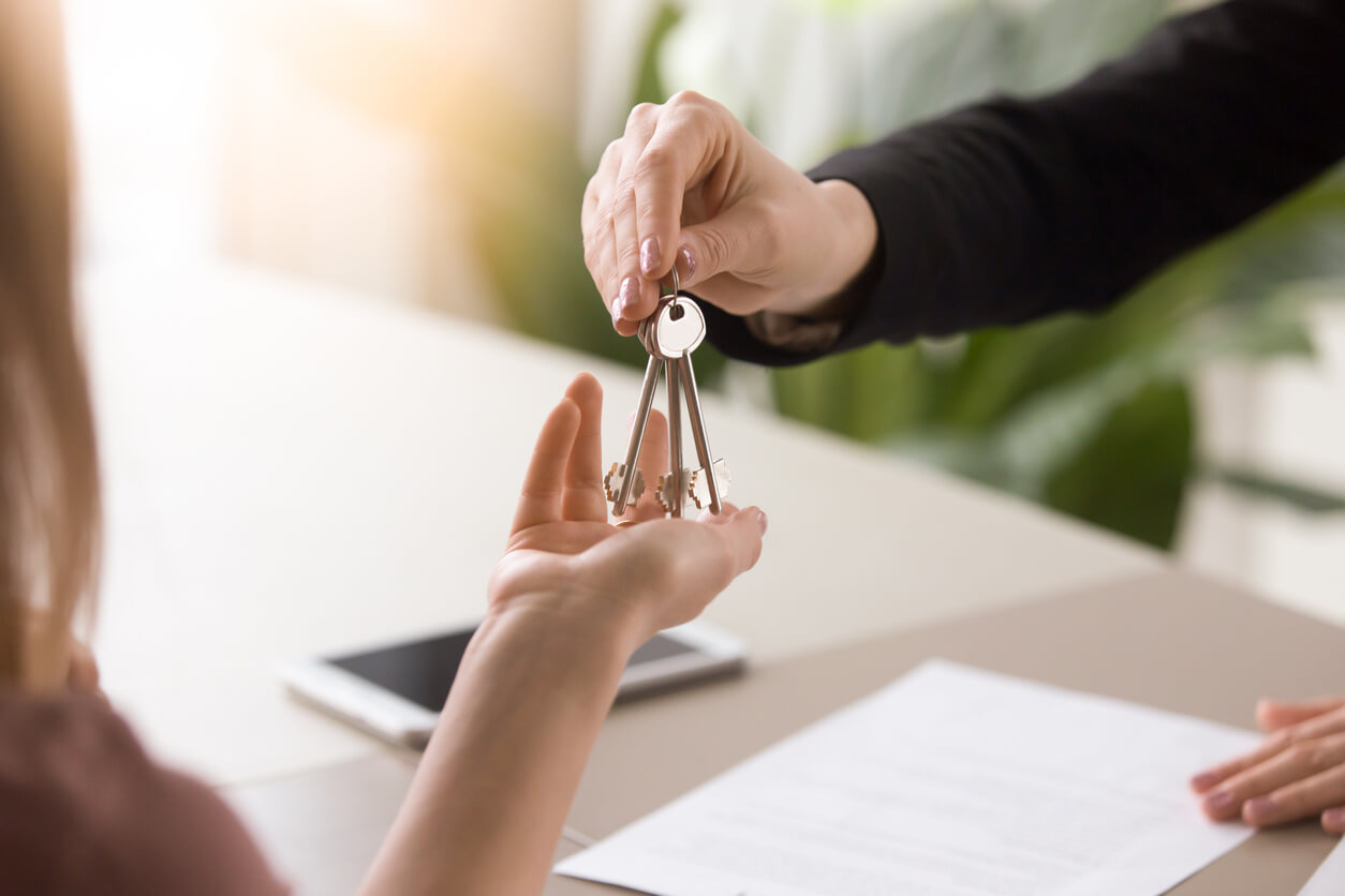 Deux personnes se tendant la main avec une clé, symbolisant l'optimisation de la fiscalité d'une SCI pour un investissement locatif rentable.